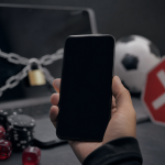 Pessoa usando celular diante de tela sem identificação visual em representação ao bloqueio de plataformas de apostas on-line