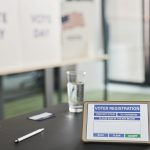 Tablet com sistema digital de registro de eleitores em uma seção eleitoral, ao lado de avisos sobre o dia da votação.