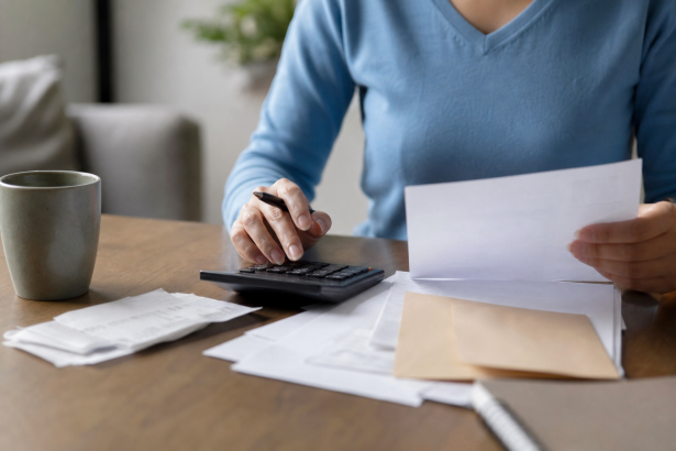 Pessoa organizando contas e documentos financeiros sobre uma mesa, sem textos legíveis ou números visíveis