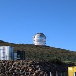 Grande cúpula de observatório científico situada no alto de uma colina sob céu azul.