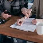 Casal analisa documentos financeiros e usa uma calculadora à mesa de casa.