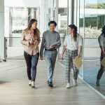 Três colegas caminham e conversam em um escritório moderno.