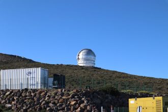 Grande cúpula de observatório científico situada no alto de uma colina sob céu azul.