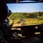 Militares observam uma atividade ao ar livre de dentro de um veículo blindado.