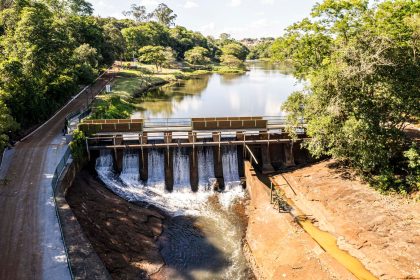 Vista aérea de uma represa cercada por um reservatório de águas tranquilas e vegetação, sob céu claro.