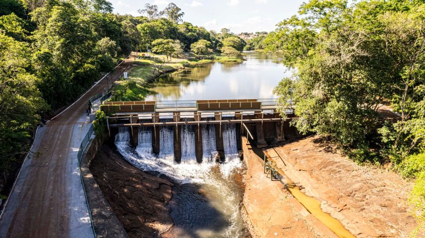 Vista aérea de uma represa cercada por um reservatório de águas tranquilas e vegetação, sob céu claro.